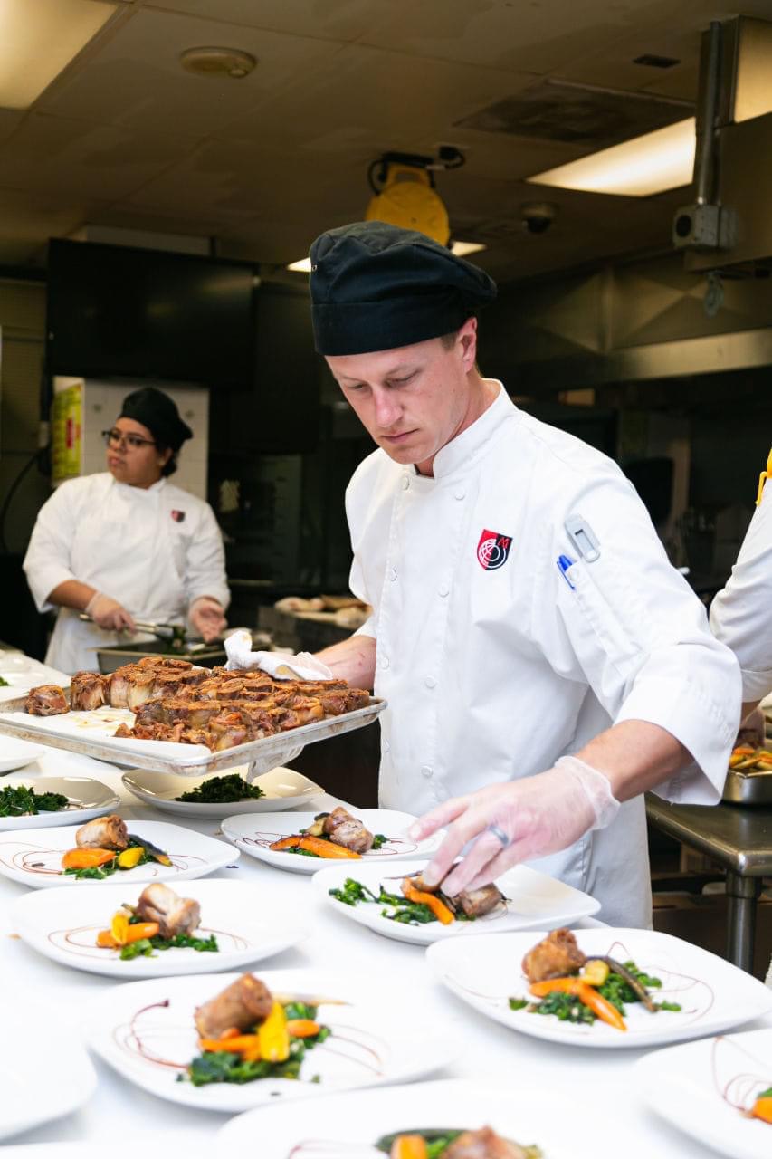 Culinary team plating crispy duck confit with greens and charred carrots